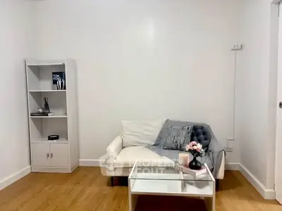 Cozy living room with modern decor and wooden flooring, featuring a white sofa and glass coffee table.
