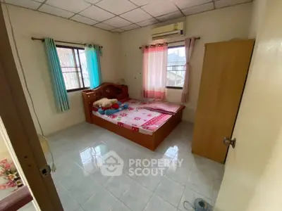 Cozy bedroom with natural light and simple decor, featuring tiled floors and air conditioning.