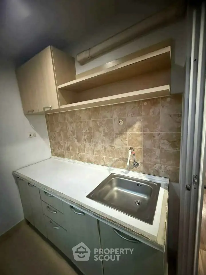 Compact kitchen with tiled backsplash and stainless steel sink, ideal for modern apartments.