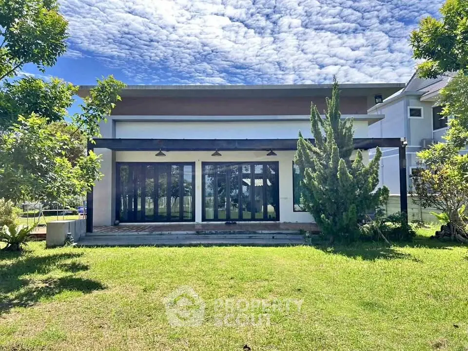 Modern house exterior with lush green lawn and large glass windows under a vibrant blue sky.