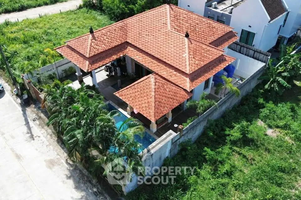 Charming villa with red-tiled roof and private pool, surrounded by lush greenery, offering serene living environment.