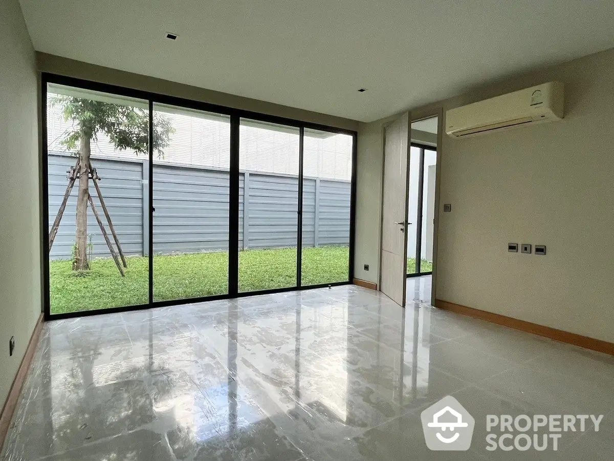 Spacious and bright living room with polished marble floors and large sliding glass doors leading to a lush garden, perfect for modern living.