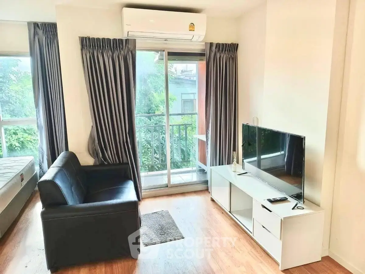 Modern living room with balcony view, featuring sleek black sofa and flat-screen TV, perfect for urban living.