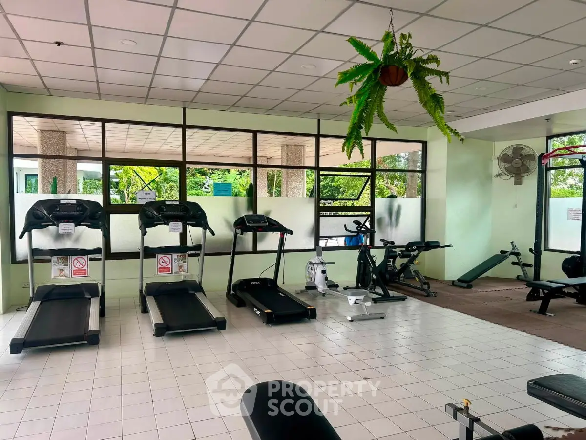 Spacious gym with modern equipment and lush outdoor views, perfect for fitness enthusiasts.