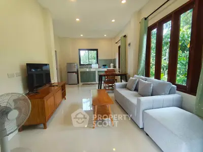 Spacious living room with modern furniture and open kitchen layout, featuring large windows and natural light.