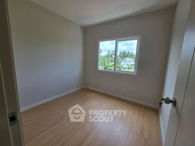 Spacious empty room with large window and wooden flooring, perfect for customization.