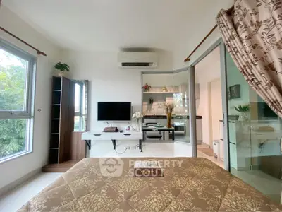 Modern bedroom with TV, air conditioning, and large windows offering natural light.