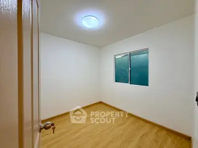 Minimalist empty room with wooden flooring and a window, perfect for customization.