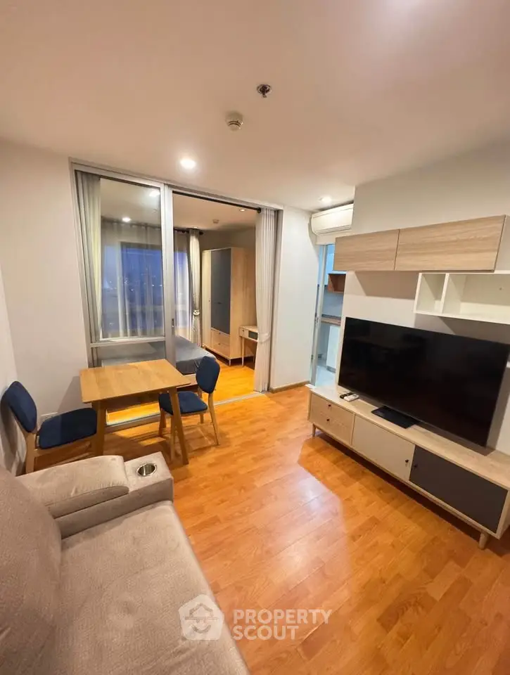 Modern living room with wooden flooring, cozy sofa, dining table, and large TV unit.