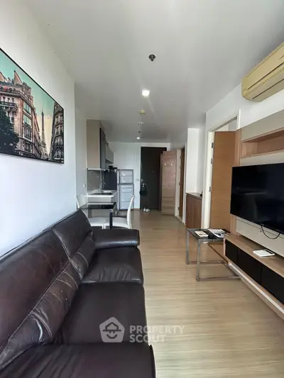 Modern living room with leather sofa, wall-mounted TV, and open kitchen layout in a stylish apartment.
