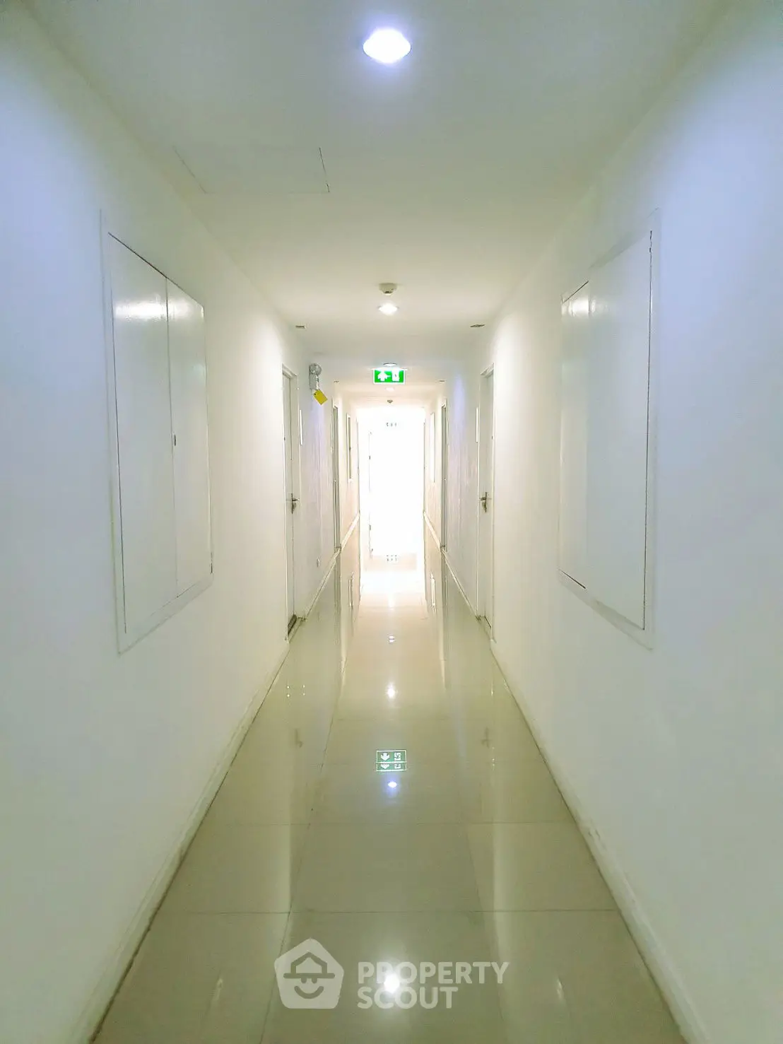 Bright and clean hallway with glossy tiled floor and emergency exit sign.