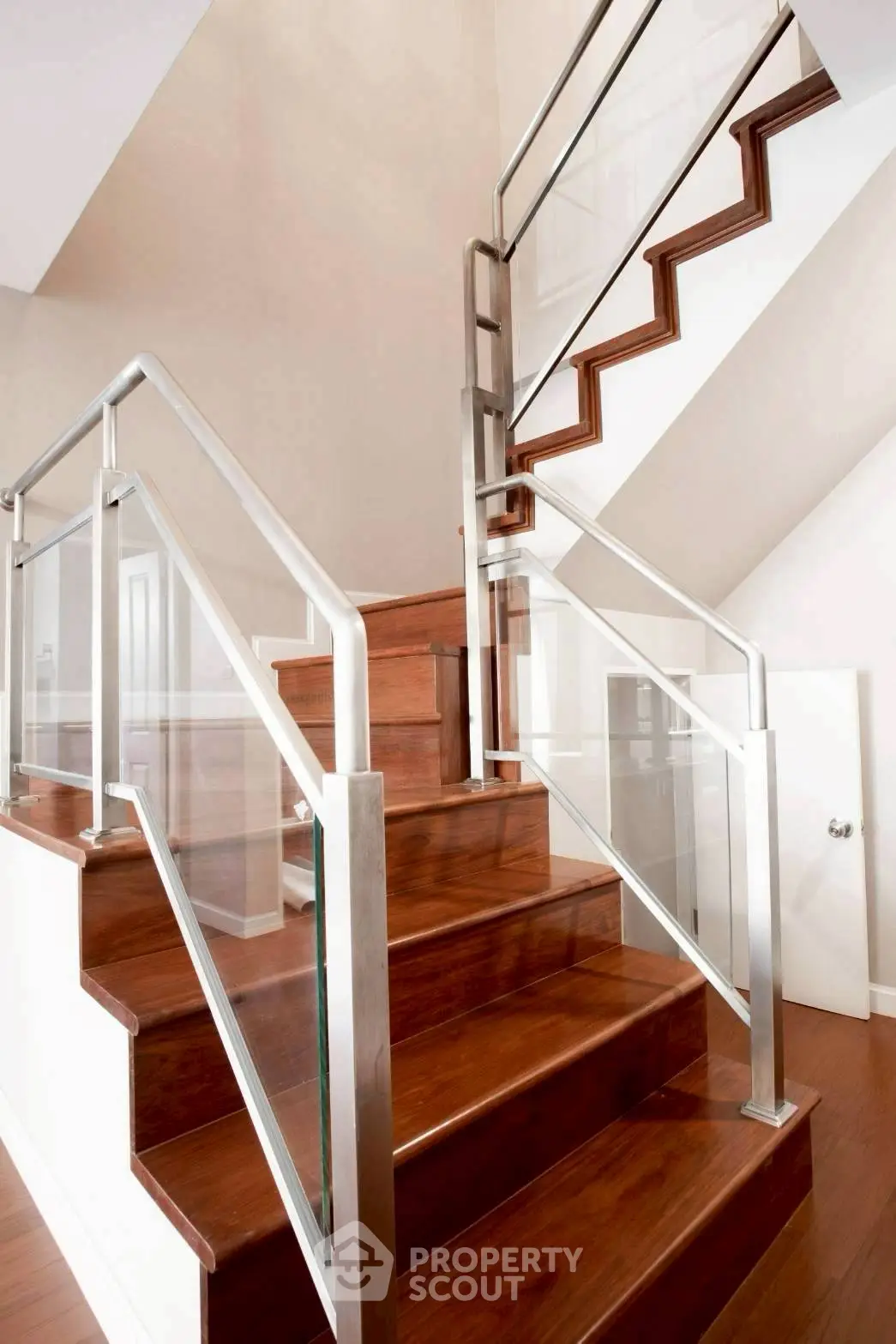 Elegant wooden staircase with modern glass railing in a bright interior space.