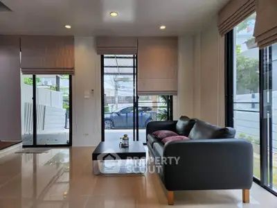 Modern living room with sleek black sofa and large windows offering natural light.