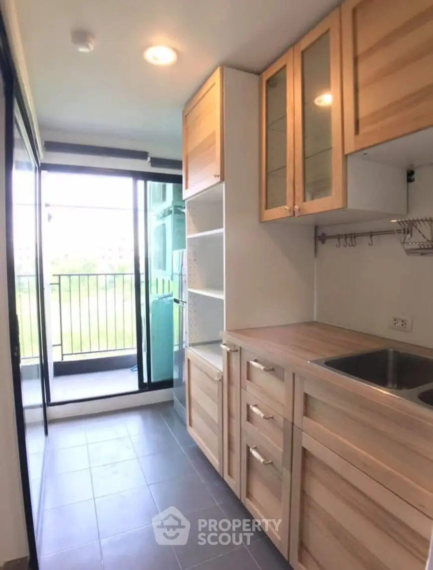 Modern kitchen with wooden cabinets and balcony access in a bright apartment.