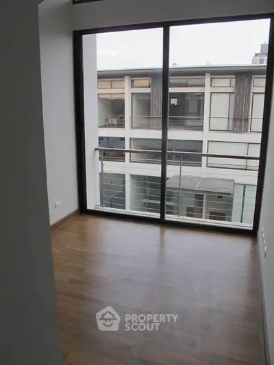 Modern apartment with large window offering courtyard view and wooden flooring.