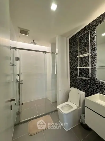 Modern bathroom with glass shower and sleek black tile accent wall.