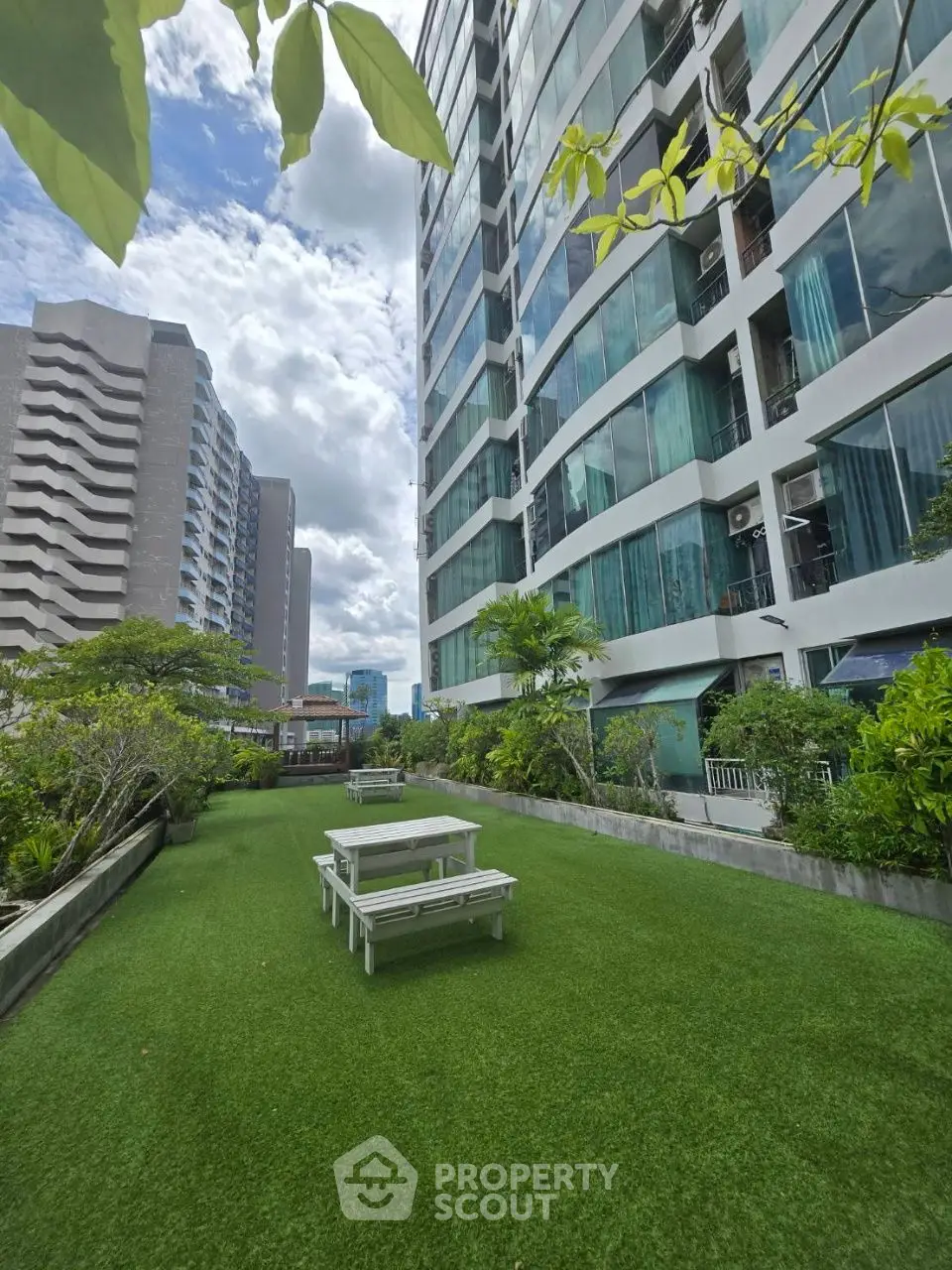 Modern high-rise building with lush garden and picnic area, perfect for urban living.