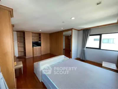 Spacious bedroom with wooden flooring and built-in storage, featuring a large window for natural light.