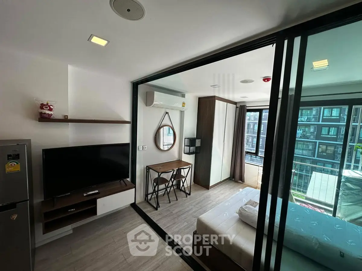 Modern studio apartment with glass partition, featuring a cozy living area and a bright bedroom with balcony view.