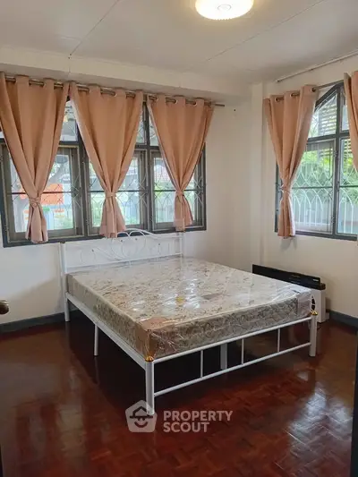 Spacious bedroom with large windows and elegant curtains, featuring a comfortable bed and polished wooden floor.