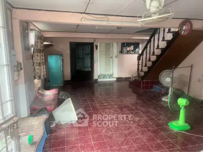 Spacious living room with vintage decor and staircase, featuring red tiled floor and ceiling fan.