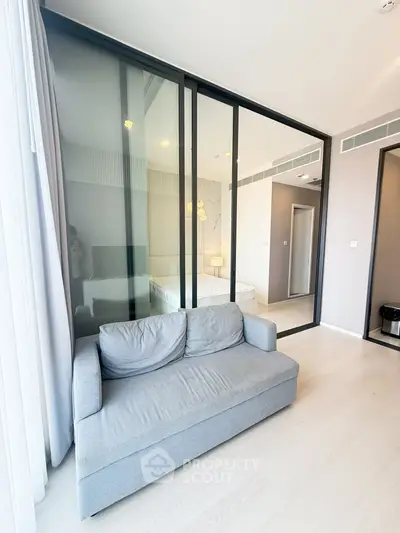 Modern apartment with glass partition separating living room and bedroom, featuring sleek design and natural light.
