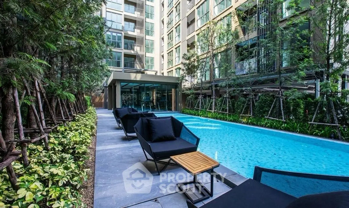 Luxurious modern apartment poolside area with stylish lounge chairs and lush greenery.