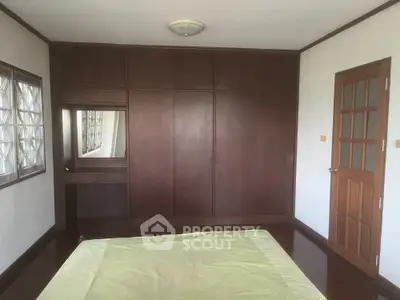Spacious bedroom with large built-in wooden wardrobe and ample natural light, featuring classic design and a cozy ambiance.