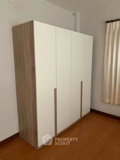 Modern minimalist wardrobe in a bright room with wooden flooring and curtains.