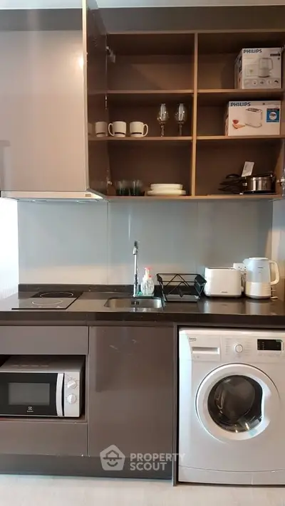 Modern kitchen with sleek appliances and open shelving, featuring a washing machine and microwave.