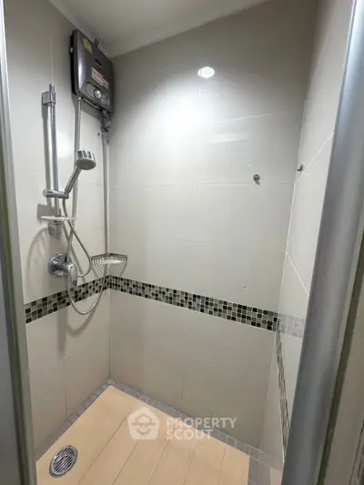 Modern shower area with sleek tiles and water heater in a compact bathroom.