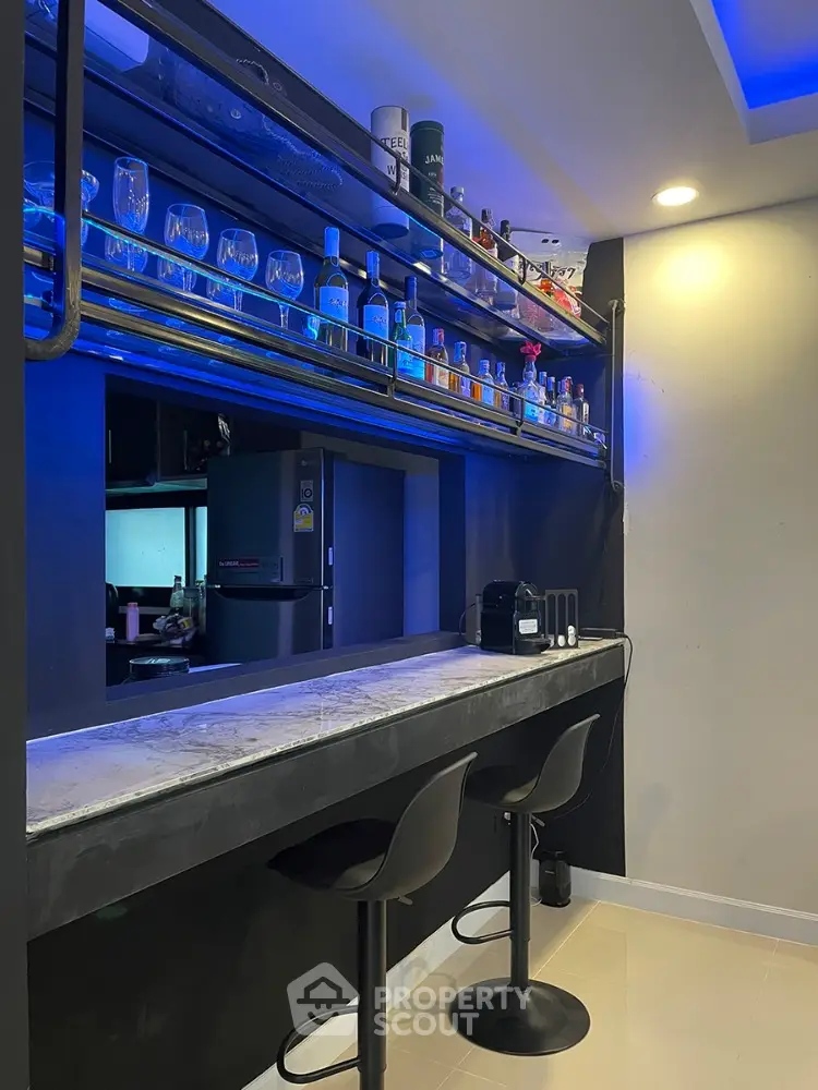 Chic home bar setup with blue accent lighting, modern bar stools, and an array of glassware and bottles on floating shelves.