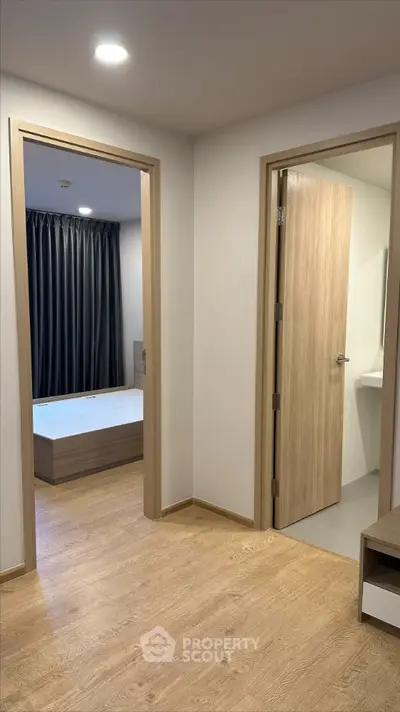 Modern apartment interior showcasing a cozy bedroom with a large bed and elegant curtains, adjacent to a sleek bathroom with a wooden door.