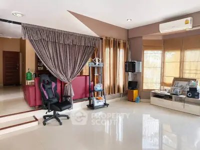 Spacious living room with modern decor and natural light, featuring a gaming chair and entertainment setup.