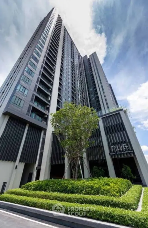 Modern high-rise building with lush landscaping and clear blue sky.