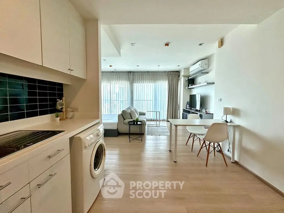 Modern open-plan living room with kitchen, featuring sleek furniture and natural light.