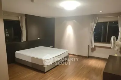 Spacious bedroom with wooden flooring and large windows for natural light.