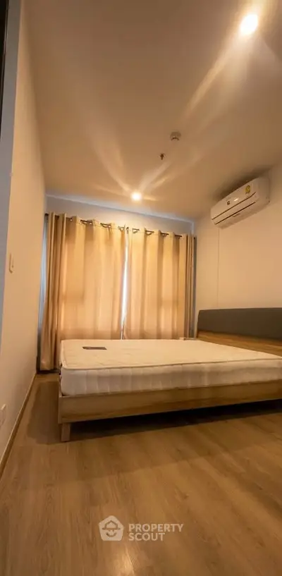 Spacious bedroom with wooden flooring and natural light, featuring a comfortable bed and air conditioning.