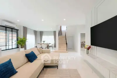 Spacious modern living room with elegant decor and open layout, featuring a cozy beige sofa and large flat-screen TV.