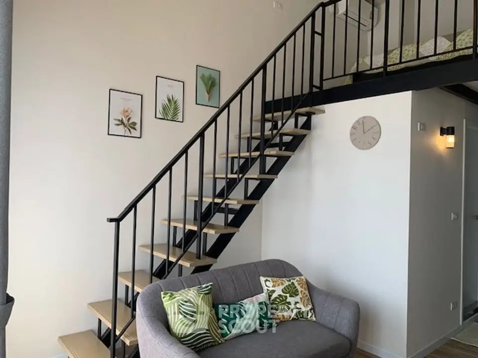 Modern loft apartment with stylish staircase and cozy living area, featuring decorative wall art and a comfortable sofa.