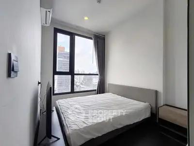 Modern bedroom with large window offering city view, featuring sleek furniture and minimalist design.