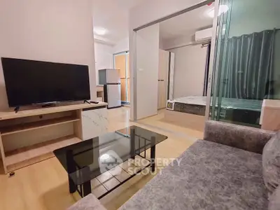 Modern living room with TV, glass coffee table, and view into bedroom