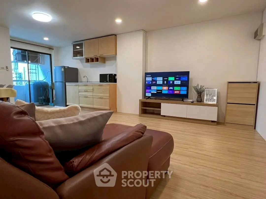 Modern living room with open kitchen and balcony view, featuring sleek furniture and smart TV.