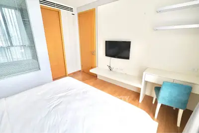 Modern bedroom with wooden flooring, wall-mounted TV, and study desk with chair.