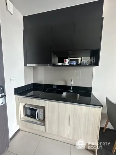 Modern compact kitchen with sleek black cabinets and built-in microwave