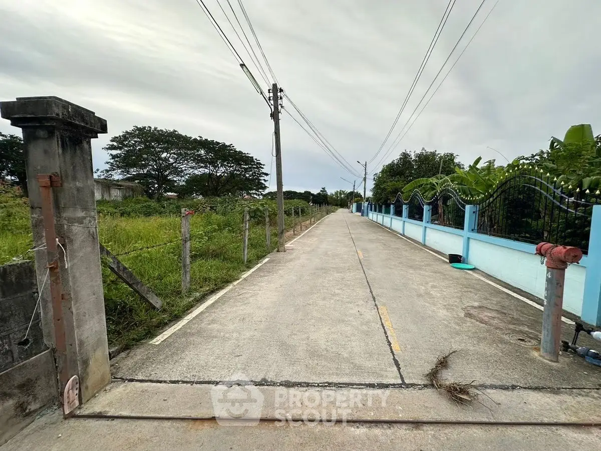 Charming rural road with lush greenery and blue fence, perfect for serene countryside living.