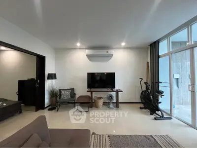 Modern living room with exercise bike and large TV, featuring sleek furniture and natural light.