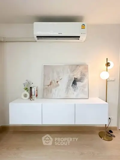 Modern living room with sleek white cabinet, stylish artwork, and elegant floor lamp under air conditioning unit.