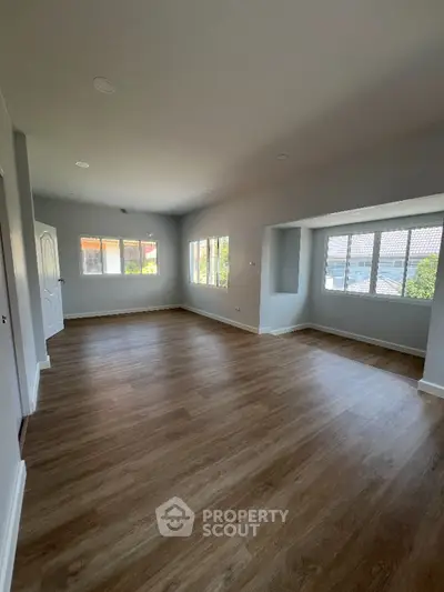 Spacious and well-lit living room with elegant hardwood flooring and multiple windows offering ample natural light, perfect for family gatherings.
