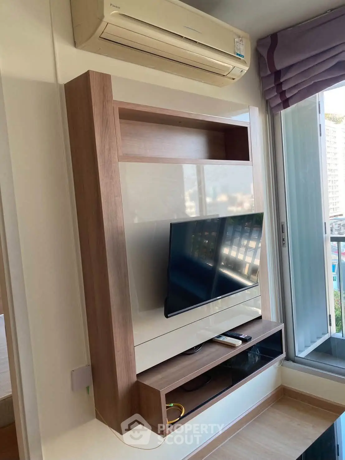 Modern living room with wall-mounted TV and air conditioning, featuring sleek wooden shelving and a glimpse of balcony view.